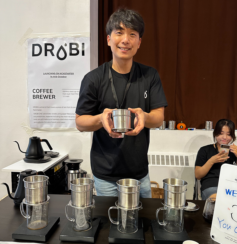 Man holding a stainless steel coffee brewer and smiling